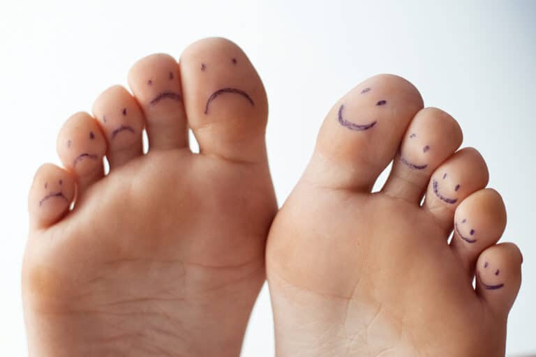 image of the underside of two feet. On one foot there is a smiley face drawn on each toe, on the other foot there is a frown face drawn on each toe